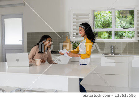 In modern kitchen, African American mother and child talking with laptop open 135635596