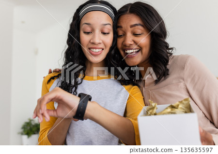 Mother and daughter excitedly exploring smartwatch features together at home 135635597