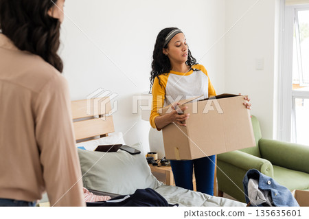 Woman carrying cardboard box in bedroom while organizing and tidying up space Woman carrying cardboard box in bedroom while organizing and tidying up space 135635601