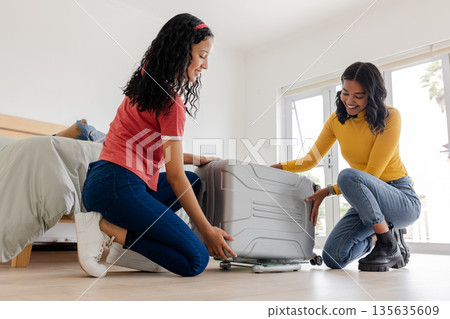 Mother and daughter packing suitcase together at home, preparing for travel 135635609