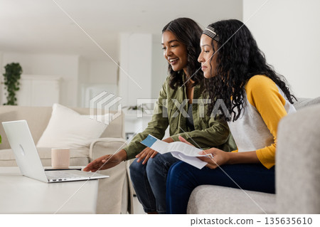 Mother and daughter using laptop at home, discussing documents and smiling 135635610