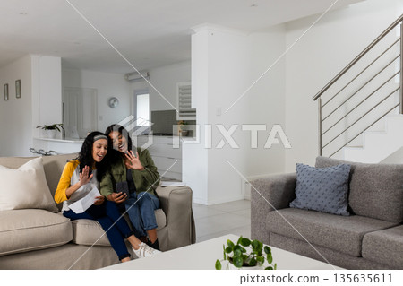 African American women sitting on sofa video calling with smartphone, smiling warmly African American women sitting on sofa video calling with smartphone, smiling warmly 135635611