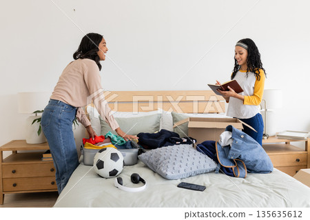 Mother and daughter organizing clothes and sports gear on bed, smiling together Mother and daughter organizing clothes and sports gear on bed, smiling together 135635612