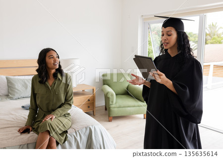 Graduate in cap and gown practicing speech with supportive mother at home 135635614