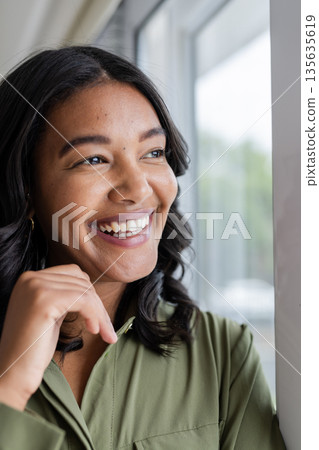 Smiling woman looking out window, enjoying peaceful moment at home 135635619