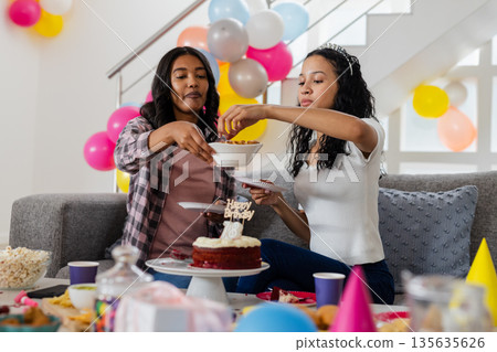 Celebrating birthday, two women enjoying snacks and cake at home party 135635626