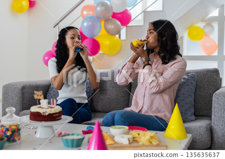 Celebrating at home, two women blowing balloons with party decorations around 135635637