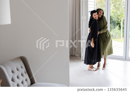 At home, African American mother hugging daughter in cap and gown for graduation 135635645