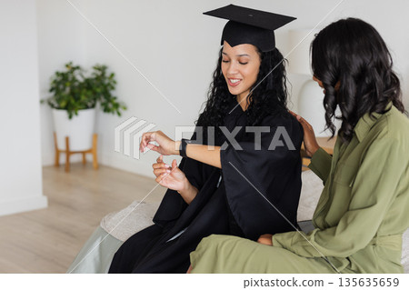 Graduation day, African American woman in cap and gown checking smartwatch, smiling Graduation day, African American woman in cap and gown checking smartwatch, smiling 135635659