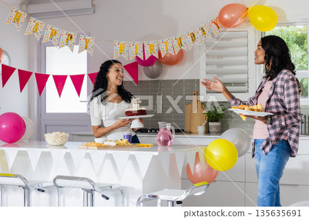 Celebrating birthday at home, two women enjoying cake and snacks with balloons Celebrating birthday at home, two women enjoying cake and snacks with balloons 135635691