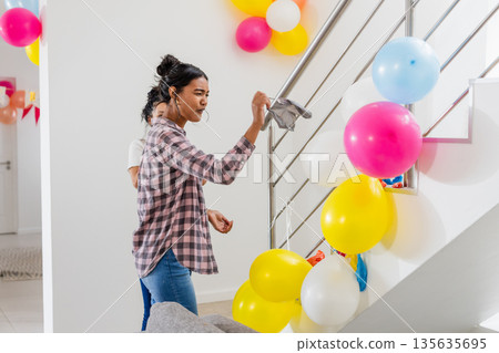 Woman decorating staircase with colorful balloons for festive home celebration Woman decorating staircase with colorful balloons for festive home celebration 135635695