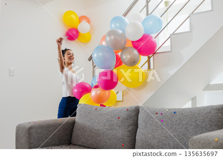 Celebrating at home, joyful woman decorating staircase with colorful balloons Celebrating at home, joyful woman decorating staircase with colorful balloons 135635697