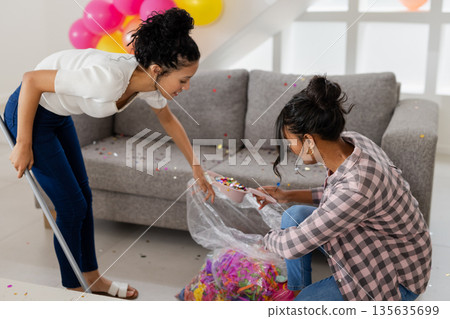 Cleaning up after party, two women gathering confetti in living room Cleaning up after party, two women gathering confetti in living room 135635699