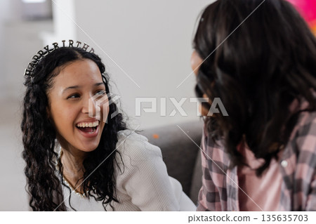 Celebrating birthday, smiling woman wearing tiara talking with friend at home Celebrating birthday, smiling woman wearing tiara talking with friend at home 135635703