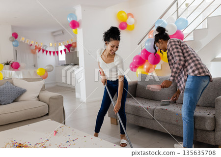 Cleaning living room after party, African American women surrounded by colorful balloons 135635708