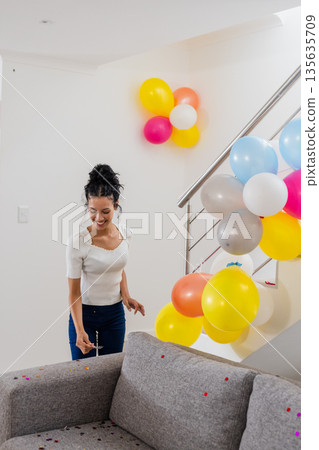 Smiling woman decorating living room with colorful balloons for celebration at home 135635709