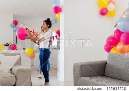 African American woman decorating living room with colorful balloons for celebration 135635718