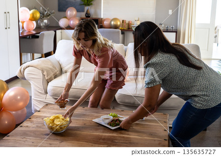 Preparing snacks and arranging decorations, women setting table for home celebration Preparing snacks and arranging decorations, women setting table for home celebration 135635727
