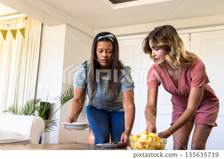 Women setting table with plates and snacks, preparing for celebration at home 135635739