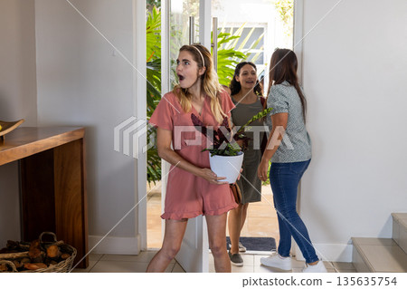 Woman holding plant, surprised as friends arrive at home for celebration Woman holding plant, surprised as friends arrive at home for celebration 135635754