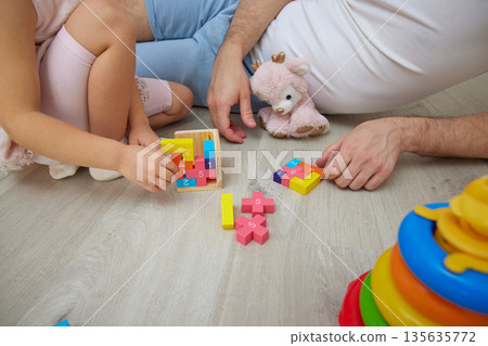 close-up of father and daughter sitting on floor at home, bonding while playing with colorful toys close-up of father and daughter sitting on floor at home, bonding while playing with colorful toys 135635772