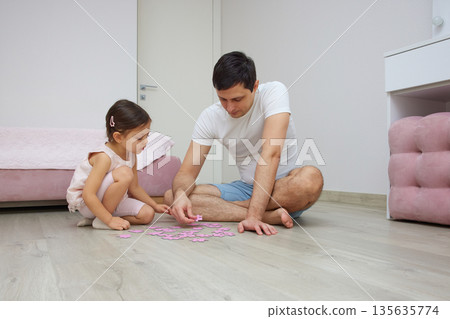 Father and daughter enjoying time together, building a puzzle on the wooden floor 135635774