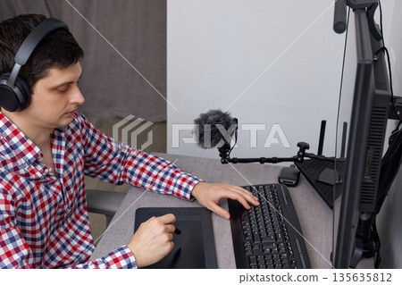 Man wearing headphones using a microphone and graphics tablet at his desk Man wearing headphones using a microphone and graphics tablet at his desk 135635812