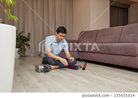 Man sitting on floor assembling parts of a vacuum cleaner Man sitting on floor assembling parts of a vacuum cleaner 135635814