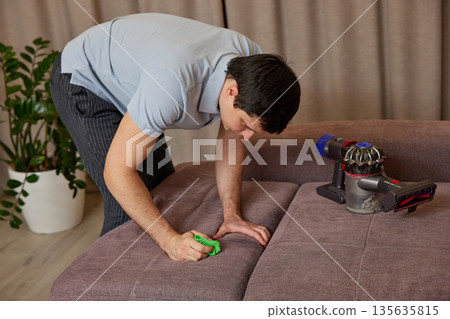 Man cleaning sofa upholstery at home using a powerful handheld vacuum cleaner 135635815