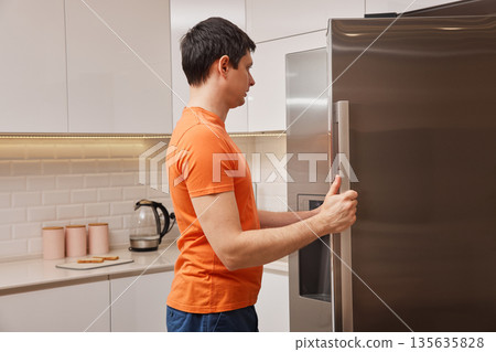 Man opens refridgerator, dealing with hunger in a home kitchen Man opens refridgerator, dealing with hunger in a home kitchen 135635828