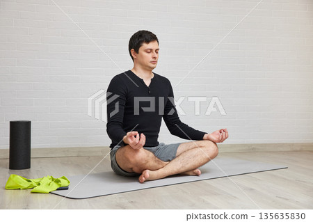 Man sitting in lotus pose on grey mat, meditating with eyes closed and hands in mudra Man sitting in lotus pose on grey mat, meditating with eyes closed and hands in mudra 135635830