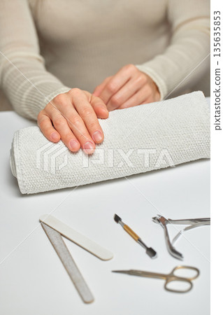 Woman's hands resting on a towel with various manicure tools on a white surface 135635853