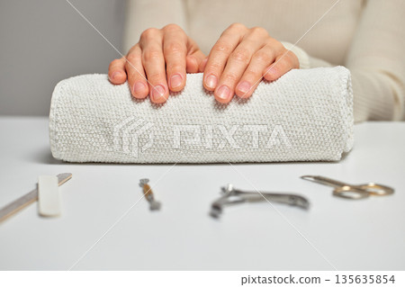 Woman hands with natural nails resting on a white towel, preparing for a manicure 135635854