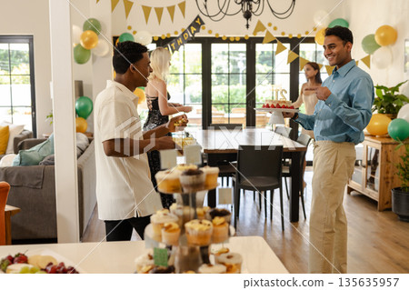 Celebrating birthday, diverse friends sharing cake and chatting in decorated room 135635957