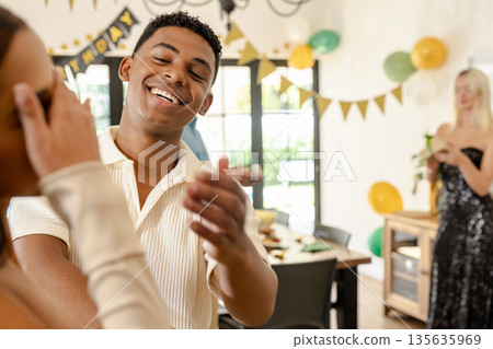 Smiling young man celebrating birthday at home with friends, enjoying moment Smiling young man celebrating birthday at home with friends, enjoying moment 135635969