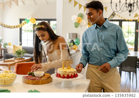 Young couple celebrating birthday at home, enjoying cake and snacks together 135635982