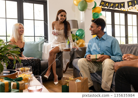 Celebrating birthday at home, friends exchanging gifts and having conversation together Celebrating birthday at home, friends exchanging gifts and having conversation together 135635984