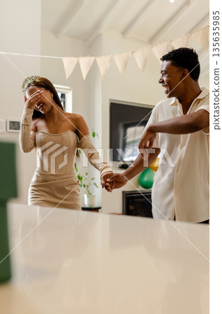 Couple celebrating birthday at home, laughing and holding hands joyfully Couple celebrating birthday at home, laughing and holding hands joyfully 135635985