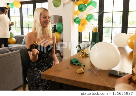 Blonde woman in black dress celebrating at home with balloons and party favors 135635987