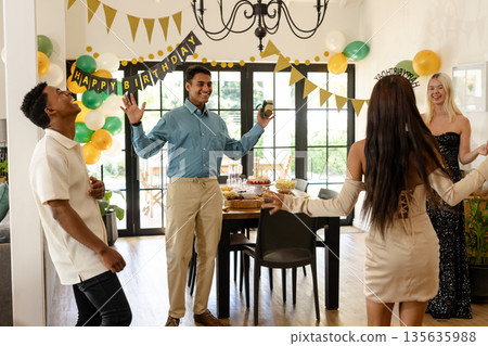 Friends celebrating birthday at home, dancing and laughing with joyful expressions 135635988