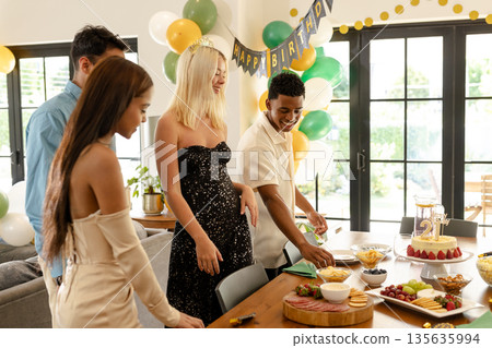 Celebrating birthday at home, friends sharing cake and snacks in festive atmosphere Celebrating birthday at home, friends sharing cake and snacks in festive atmosphere 135635994