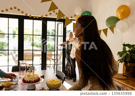 Young woman celebrating 21st birthday blowing out candles on cake at home 135635998