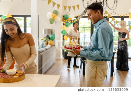 Friends celebrating birthday at home, enjoying snacks and cake with decorations 135635999