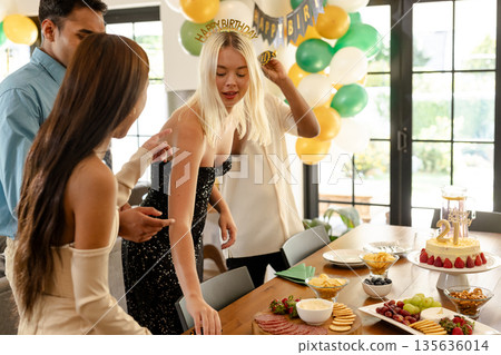 Friends celebrating birthday with snacks and cake in decorated living room Friends celebrating birthday with snacks and cake in decorated living room 135636014