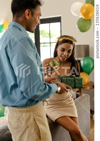 Celebrating birthday, woman opening gift box with friend at home, smiling happily Celebrating birthday, woman opening gift box with friend at home, smiling happily 135636019