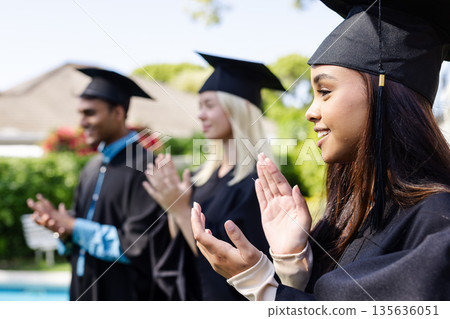Graduates in caps and gowns clapping outdoors, celebrating academic achievement Graduates in caps and gowns clapping outdoors, celebrating academic achievement 135636051