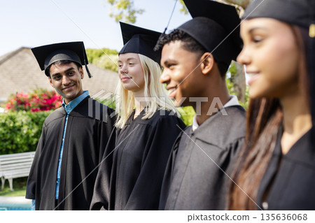 Graduating students in caps and gowns smiling outdoors, celebrating achievement 135636068