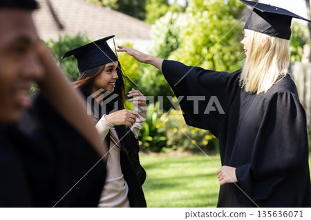 Graduating students in caps and gowns celebrating joyfully outdoors, smiling together 135636071