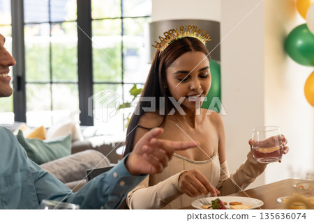 Woman wearing party headband enjoying meal and drink at festive gathering Woman wearing party headband enjoying meal and drink at festive gathering 135636074
