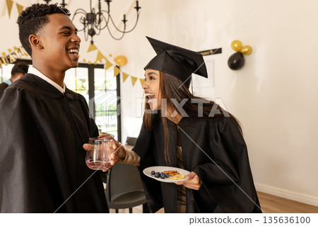 Graduates in caps and gowns celebrating with snacks and drinks at party 135636100